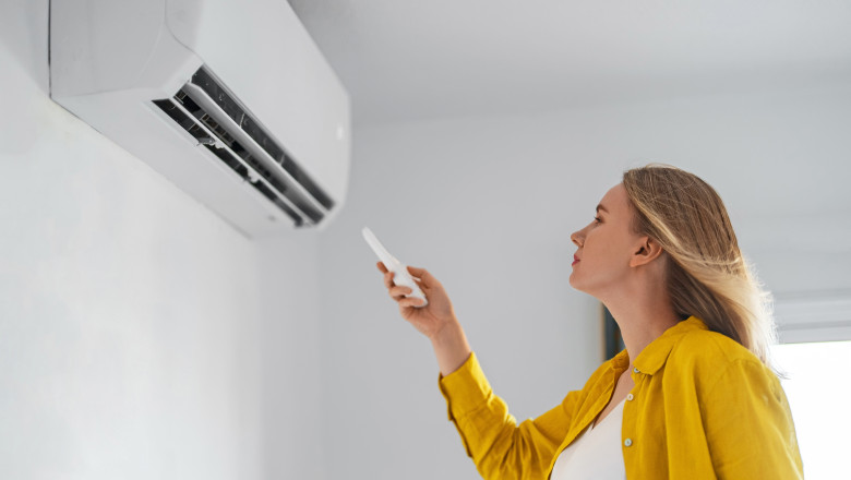 Woman,Holding,Remote,Control,Aimed,At,The,Air,Conditioner.