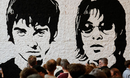Oasis fans take photos in front of the Wonder Wall - a mural by Welsh artist Nathan Wyburn made out of 3,000 black and white bucket hats depicting Liam and Noel Gallagher - at the St David's shopping centre in Cardiff, ahead of the first show in the band'