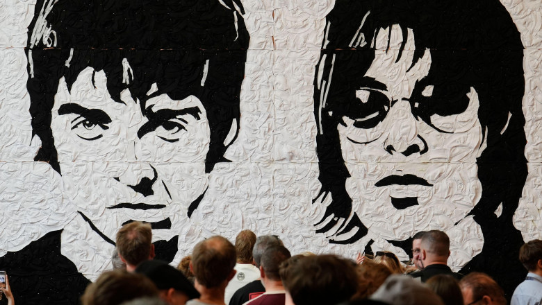 Oasis fans take photos in front of the Wonder Wall - a mural by Welsh artist Nathan Wyburn made out of 3,000 black and white bucket hats depicting Liam and Noel Gallagher - at the St David's shopping centre in Cardiff, ahead of the first show in the band'