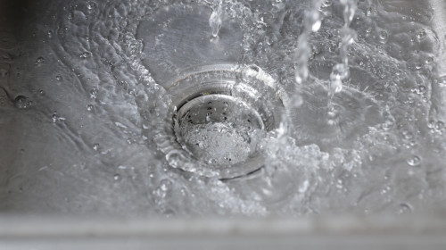 Water from the faucet flows into the sink. Water is draining into the sink.