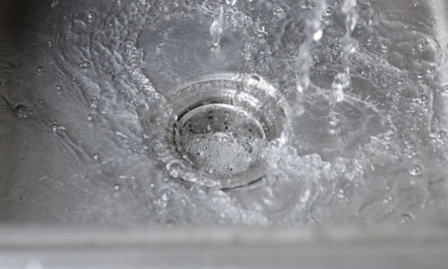 Water from the faucet flows into the sink. Water is draining into the sink.