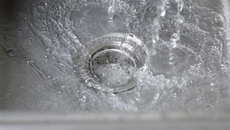 Water from the faucet flows into the sink. Water is draining into the sink.