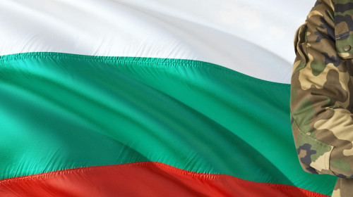 Crossed arms Bulgarian soldier with national waving flag on background - Bulgaria Military theme.