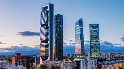 Cityscape of Madrid’s financial district at dusk, featuring modern skyscrapers illuminated against the fading evening sky. This area on the North of t