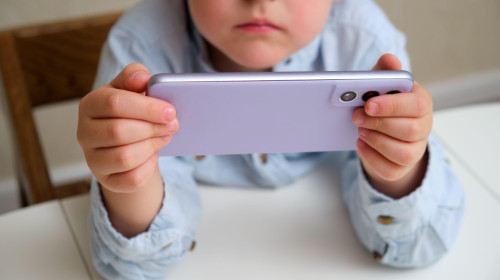 Child, a white boy, holding a purple phone in horizontal position, focus on device. Screen time concept for kids, digital childhood, online education.