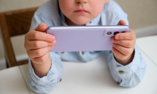 Child, a white boy, holding a purple phone in horizontal position, focus on device. Screen time concept for kids, digital childhood, online education.