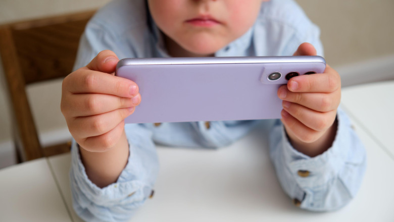 Child, a white boy, holding a purple phone in horizontal position, focus on device. Screen time concept for kids, digital childhood, online education.