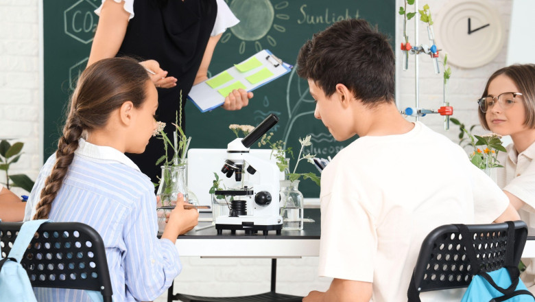 Pupils with microscope on table in Biology class at school, back view