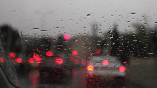 Out of focus cars, their back lights on, traffic lights, traffic on a wet Jerusalem road, rainy day as seen through rain drops on front windshield.