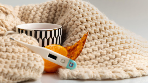 Flu and cold medicines laid out on the table, a thermometer to measure temperature, warming tea, a winter scarf wrapped around a cup, a flu epidemic,