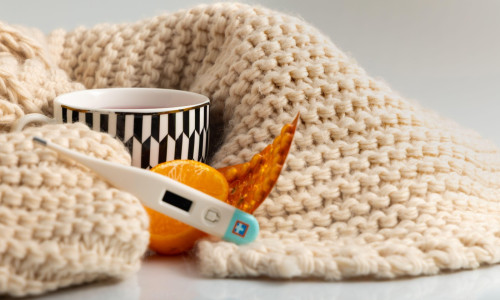 Flu and cold medicines laid out on the table, a thermometer to measure temperature, warming tea, a winter scarf wrapped around a cup, a flu epidemic,