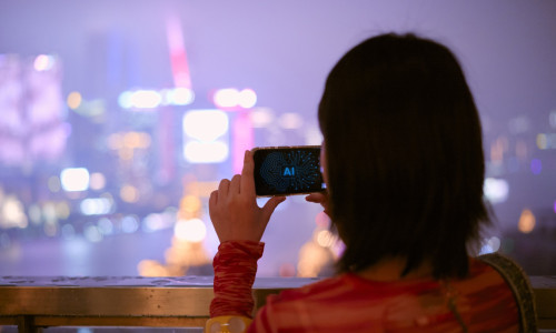 Woman capturing cityscape on AI phone at night with vibrant lights in the background. Shanghai, China