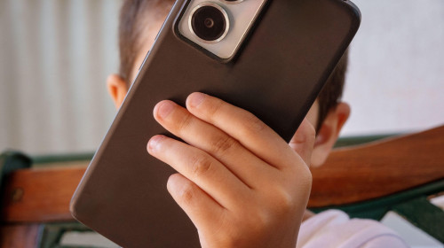 Child's face hidden by a smartphone, concept of screen time and online safety. Anonymous kid holding a mobile phone illustrates digital addiction, cyb