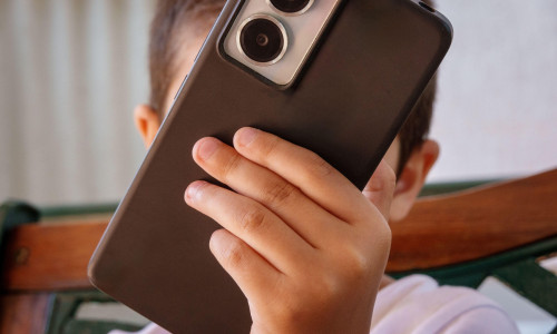 Child's face hidden by a smartphone, concept of screen time and online safety. Anonymous kid holding a mobile phone illustrates digital addiction, cyb