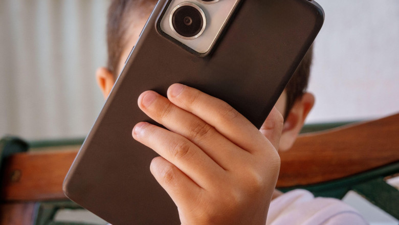 Child's face hidden by a smartphone, concept of screen time and online safety. Anonymous kid holding a mobile phone illustrates digital addiction, cyb