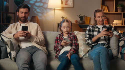 Family mother father daughter girl kid child parents man woman relaxing in home night evening on couch using mobile phones apps social media scrolling