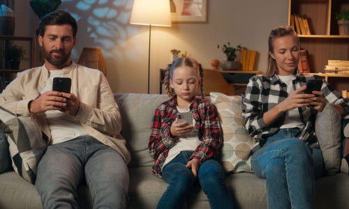 Family mother father daughter girl kid child parents man woman relaxing in home night evening on couch using mobile phones apps social media scrolling