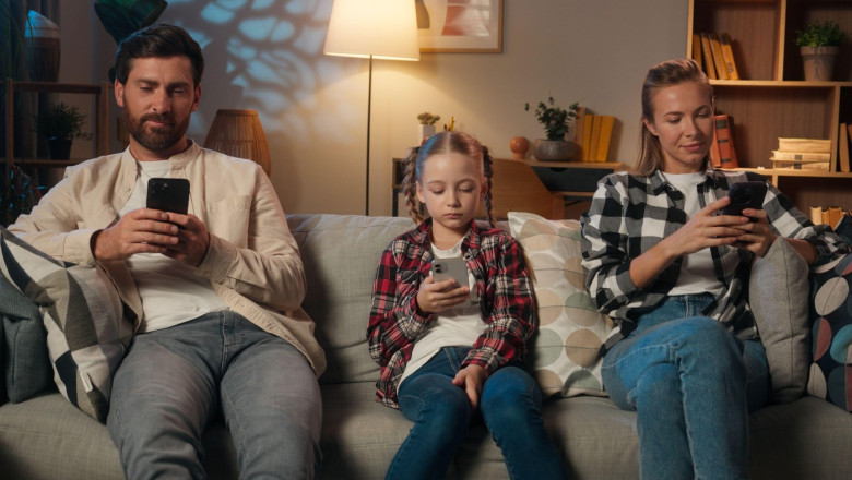 Family mother father daughter girl kid child parents man woman relaxing in home night evening on couch using mobile phones apps social media scrolling