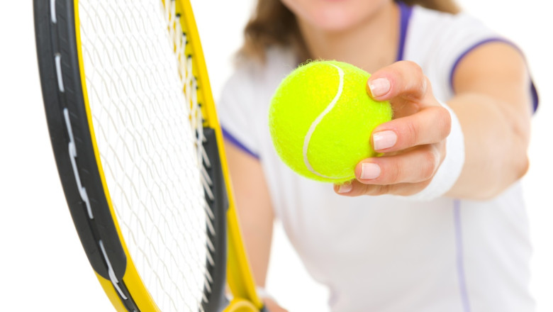 Closeup on racket and ball in hand of tennis player ready to serve