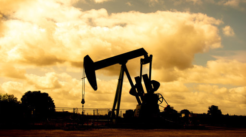 Crude oil extraction from an oil field. Pumpjack silhouetted against a background of clouds at sunset. Concepts of petroleum industry and oil prices