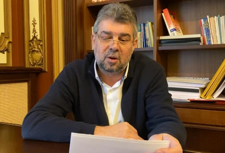 Marcel Ciolacu, citește de pe foi lângă o bibliotecă