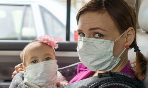 Femeie cu copil în brațe, ambii cu măști sanitare pe timp de coronavirus, COVID-19