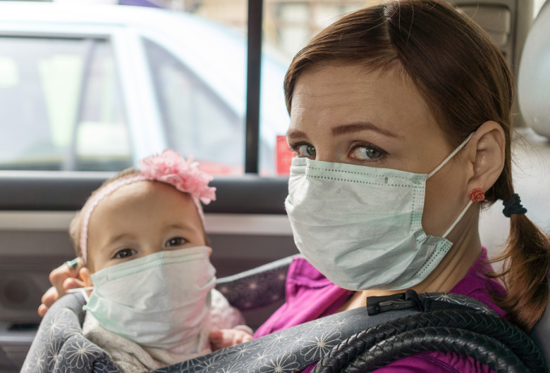 Femeie cu copil în brațe, ambii cu măști sanitare pe timp de coronavirus, COVID-19