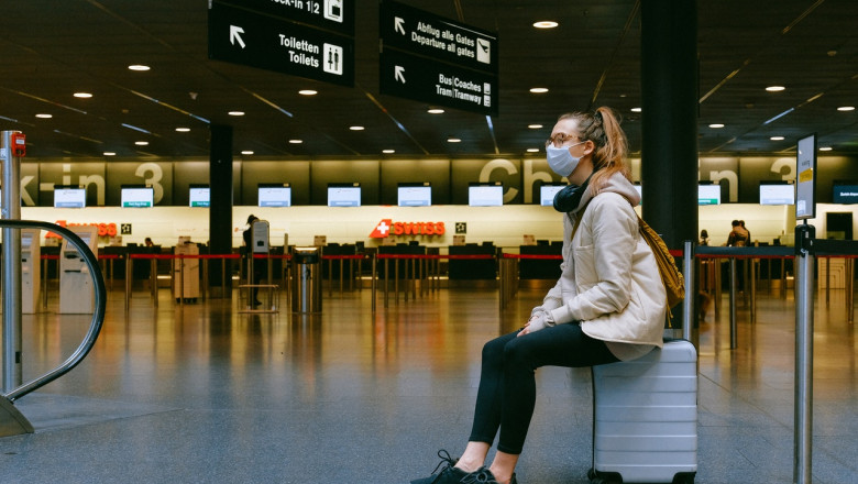 Femeie stă pe bagaj cu masca sanitară pe față, călătorie, turism în vremea COVID-19, coronavirus, aeroport