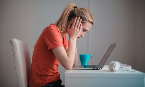 Femeie tânără se uită tristă, îngrijorată, temătoare la laptop, calculator, dată afară, concediată, necaz