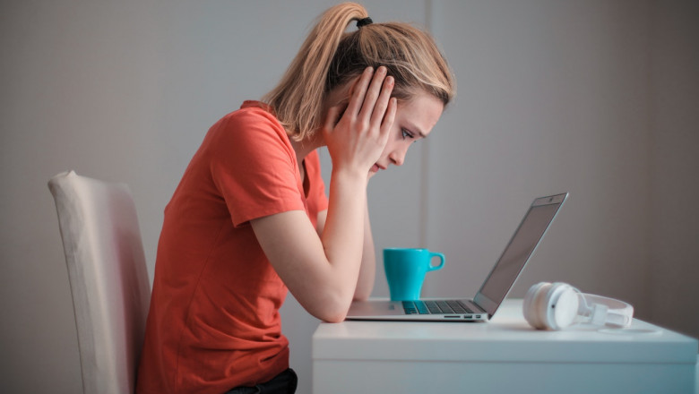 Femeie tânără se uită tristă, îngrijorată, temătoare la laptop, calculator, dată afară, concediată, necaz