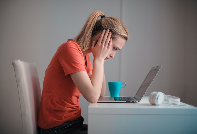 Femeie tânără se uită tristă, îngrijorată, temătoare la laptop, calculator, dată afară, concediată, necaz