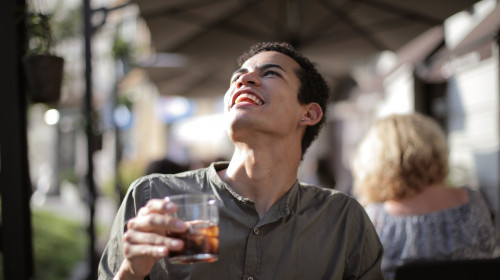 Bărbat tânăr stă la o terasă cu un pahar de băutură în mână
