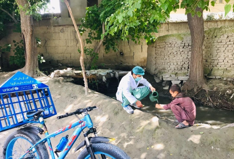 UNICEF, medic cu mască de protecție pe față toarnă apă unui copil sărac