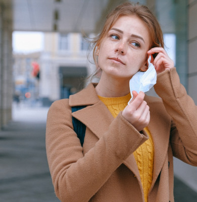 Femeie tânără își scoate masca de protecție împotriva noului coronavirus, COVID-19, cu zâmbet
