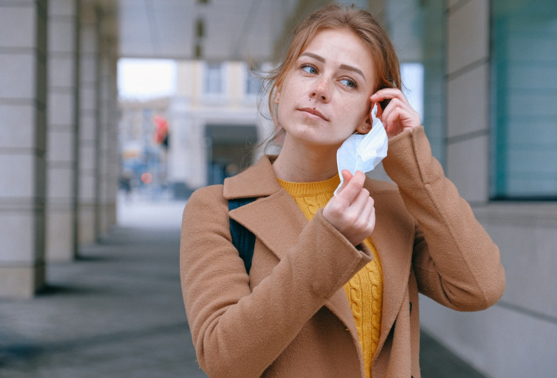 Femeie tânără își scoate masca de protecție împotriva noului coronavirus, COVID-19, cu zâmbet
