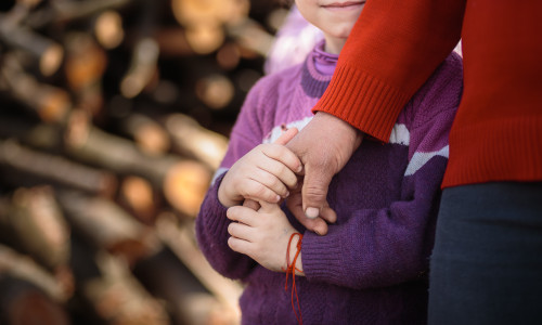 Copil sărac se ține de mâna părintelui, familie nevoiașă, sărăcie, UNICEF