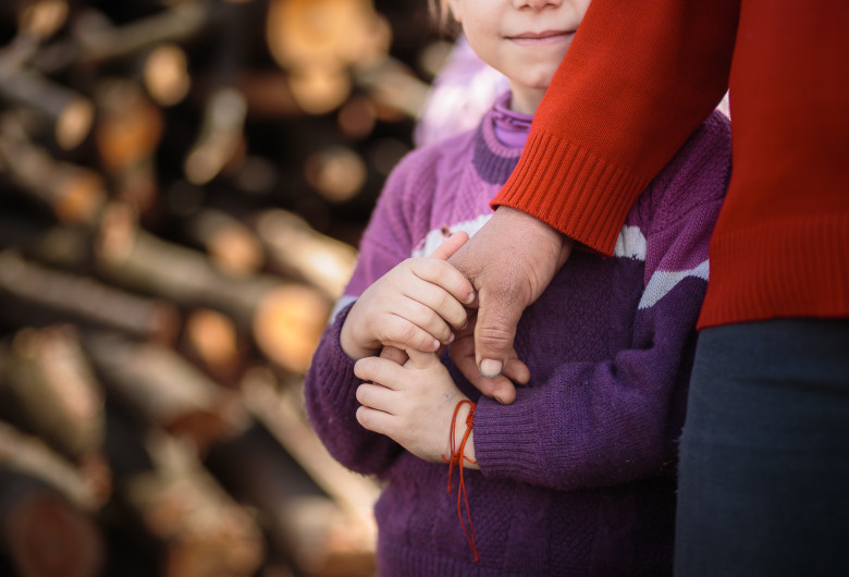 Copil sărac se ține de mâna părintelui, familie nevoiașă, sărăcie, UNICEF