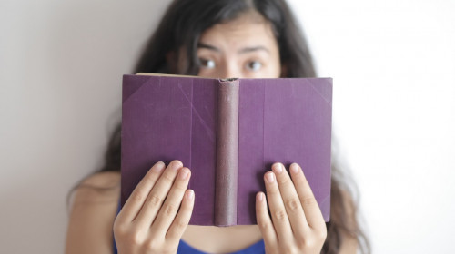 Fată care se uită mirată într-o carte, elevă, citit