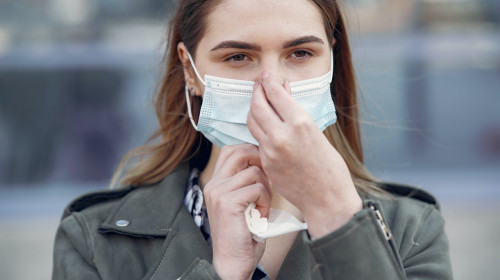 Femeie își pune mască de protecție pe față în pandemia de COVID-19, coronavirus