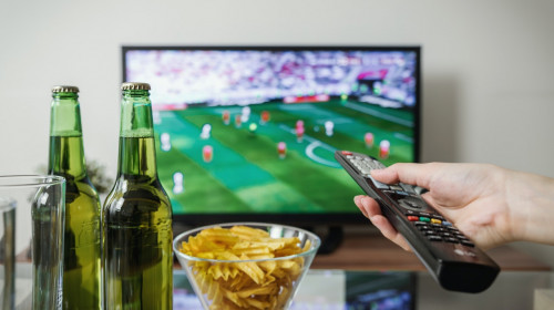 Meci de fotbal cu bere și chipsuri în fața televizorului și cu telecomandă, suporter