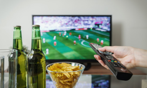 Meci de fotbal cu bere și chipsuri în fața televizorului și cu telecomandă, suporter