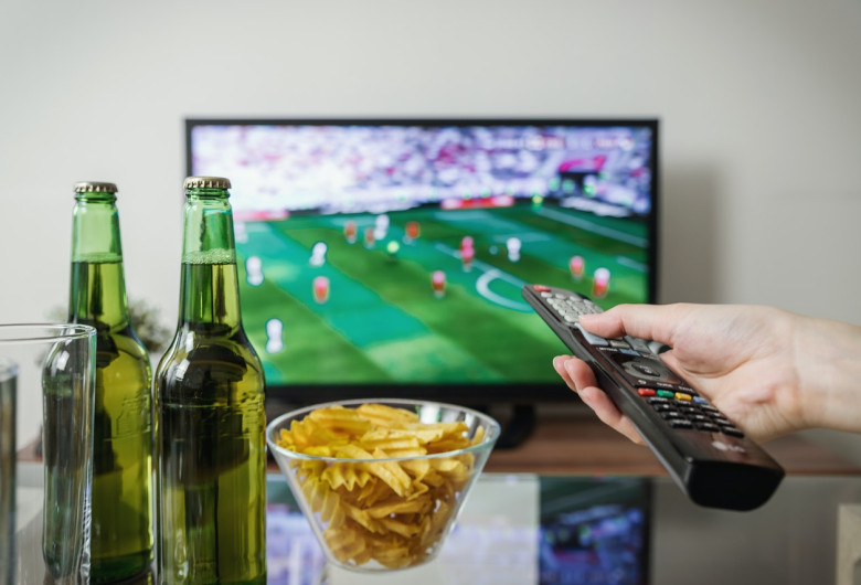 Meci de fotbal cu bere și chipsuri în fața televizorului și cu telecomandă, suporter