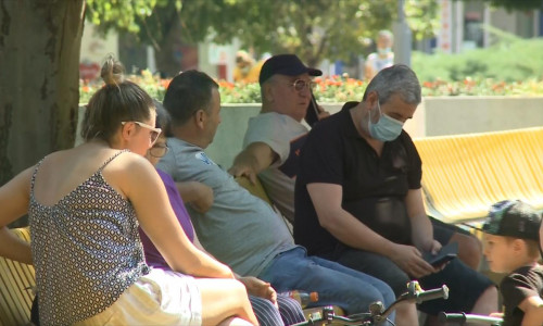 Oameni pe bancă, se relaxează în parc, unii cu mască alții fără