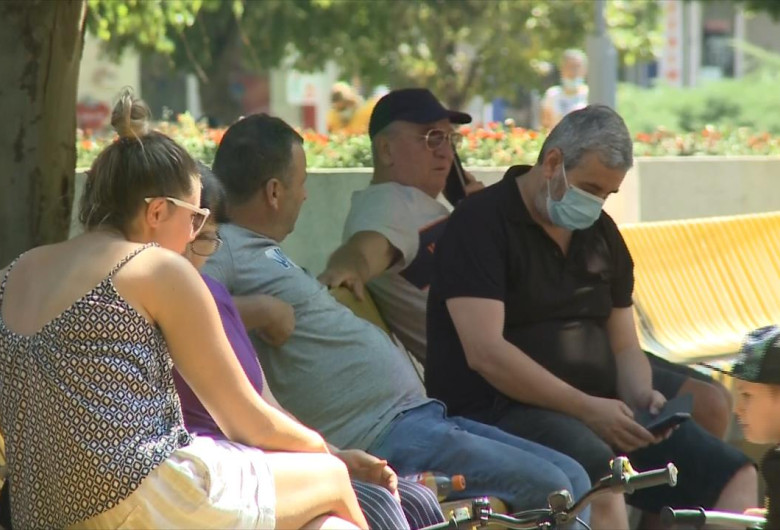 Oameni pe bancă, se relaxează în parc, unii cu mască alții fără