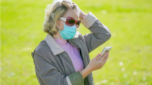 Femeie babă cu mască de coronavirus, COVID-19, SARS-CoV-2 se uită îngrijorată, temătoare în telefonul mobil la un SMS cu internet online, gadget