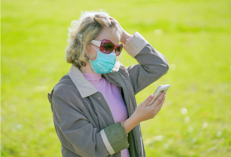 Femeie babă cu mască de coronavirus, COVID-19, SARS-CoV-2 se uită îngrijorată, temătoare în telefonul mobil la un SMS cu internet online, gadget