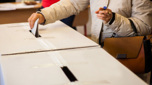 Femeie bagă buletinul de vot în urnă la secția de votare pentru alegeri, scrutin, referendum