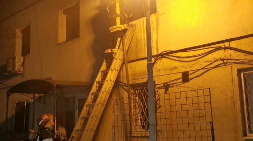 Pompier pe o scară stingând un incendiu la un bloc, seara, noaptea