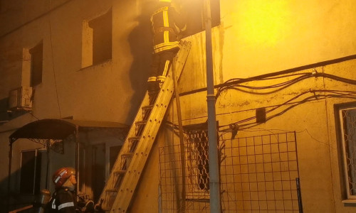 Pompier pe o scară stingând un incendiu la un bloc, seara, noaptea
