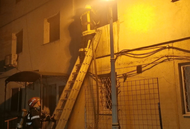 Pompier pe o scară stingând un incendiu la un bloc, seara, noaptea